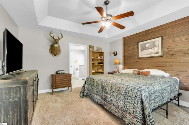 bedroom featuring light colored carpet, a raised ceiling, baseboards, ceiling fan, and wooden walls
