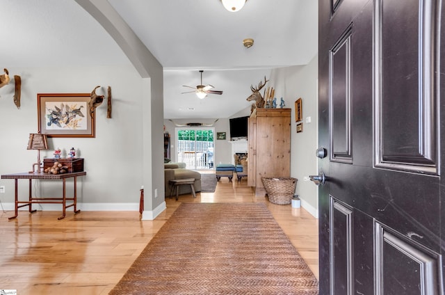 foyer featuring a ceiling fan, light wood finished floors, arched walkways, and baseboards