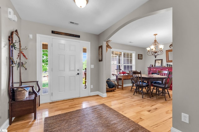 foyer entrance featuring arched walkways, light wood-type flooring, a chandelier, and baseboards