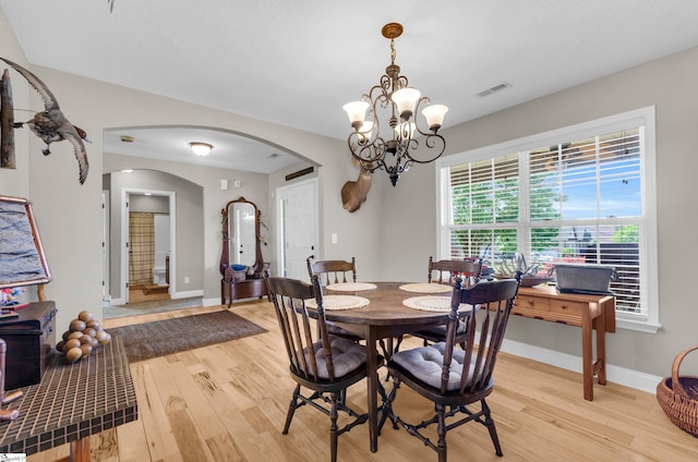 dining room featuring arched walkways, a chandelier, light wood-style floors, and baseboards