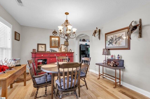dining area featuring arched walkways, light wood-style floors, and baseboards