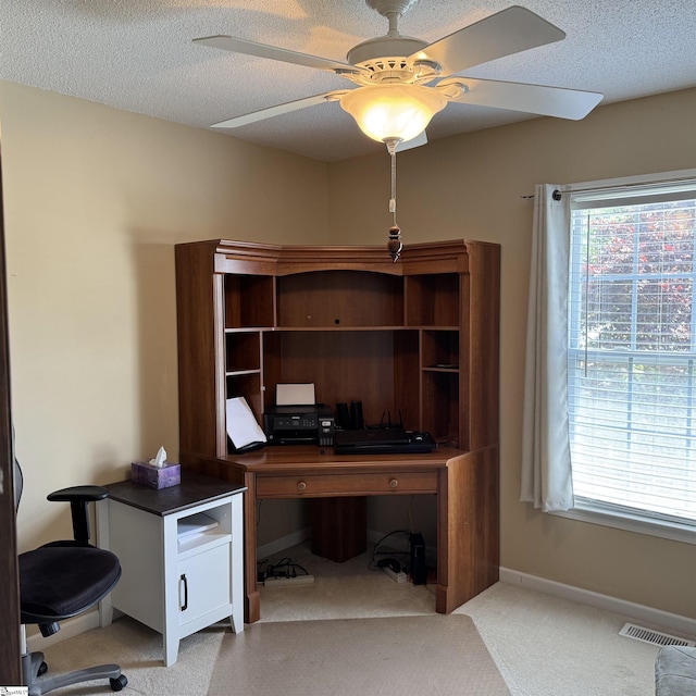 office space featuring light carpet, plenty of natural light, ceiling fan, baseboards, and a textured ceiling