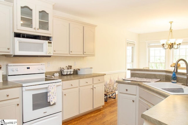 kitchen featuring white appliances, a sink, a chandelier, light wood-style flooring, and hanging light fixtures
