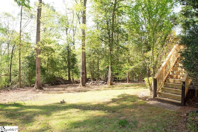 view of grassy yard featuring stairway and a forest view