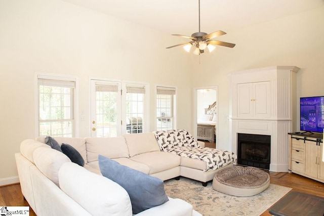 living room with ceiling fan, wood finished floors, a fireplace with flush hearth, a towering ceiling, and baseboards