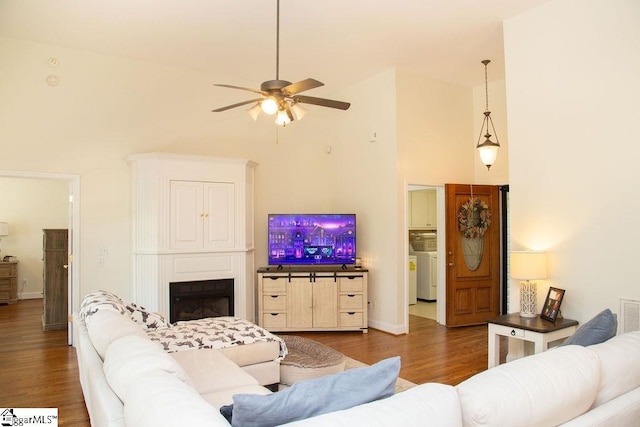 living area featuring a high ceiling, a ceiling fan, wood finished floors, washer / dryer, and a fireplace