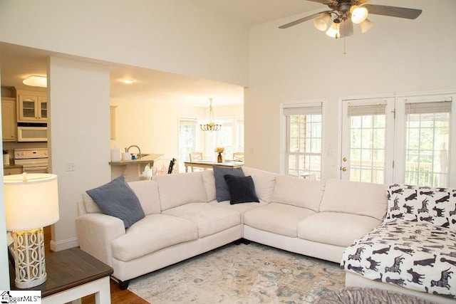 living room featuring ceiling fan, a chandelier, a towering ceiling, wood finished floors, and baseboards
