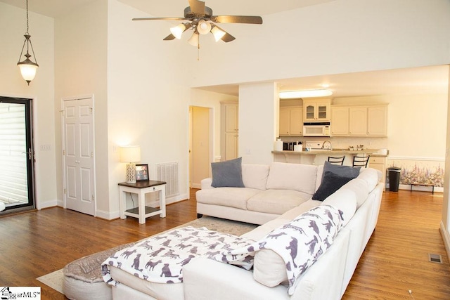 living area with high vaulted ceiling, wood finished floors, ceiling fan, and baseboards