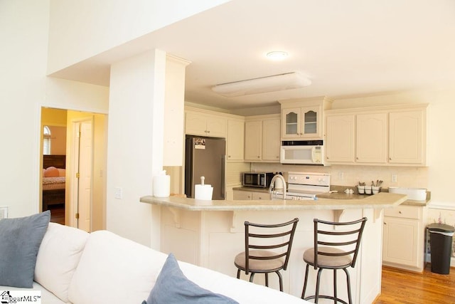 kitchen with appliances with stainless steel finishes, a breakfast bar, a peninsula, backsplash, and glass insert cabinets