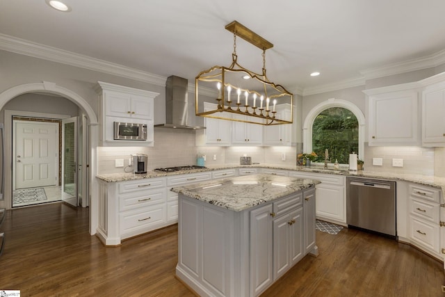 kitchen featuring appliances with stainless steel finishes, wall chimney range hood, white cabinetry, a sink, and ornamental molding