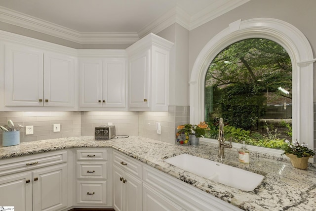 kitchen featuring a sink, white cabinets, decorative backsplash, light stone counters, and crown molding