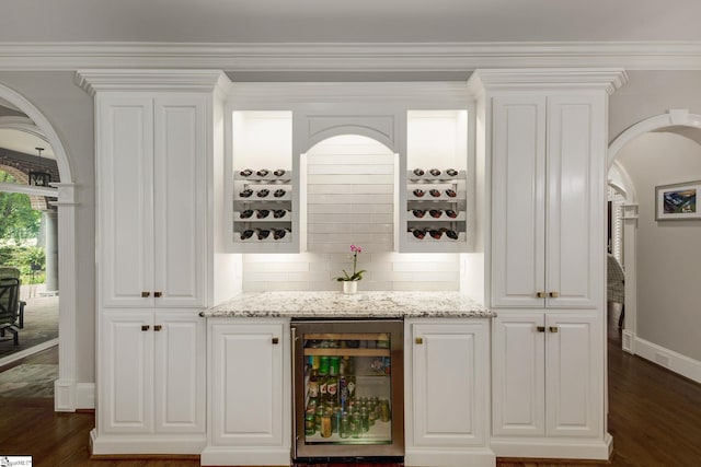 indoor dry bar featuring beverage cooler, baseboards, dark wood-type flooring, decorative backsplash, and arched walkways