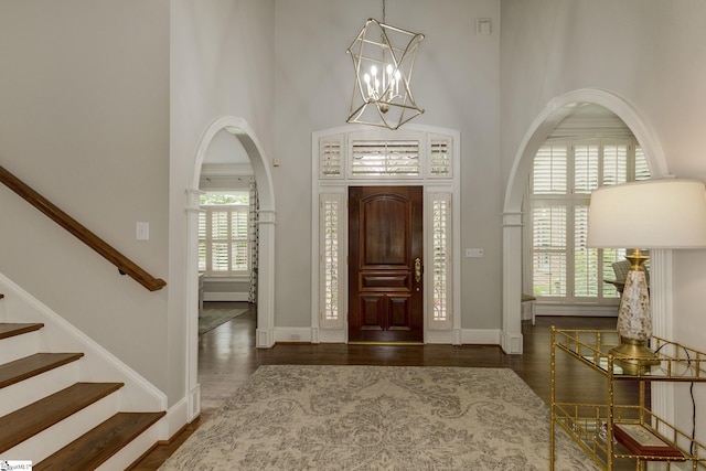 foyer with arched walkways, a high ceiling, wood finished floors, a chandelier, and baseboards