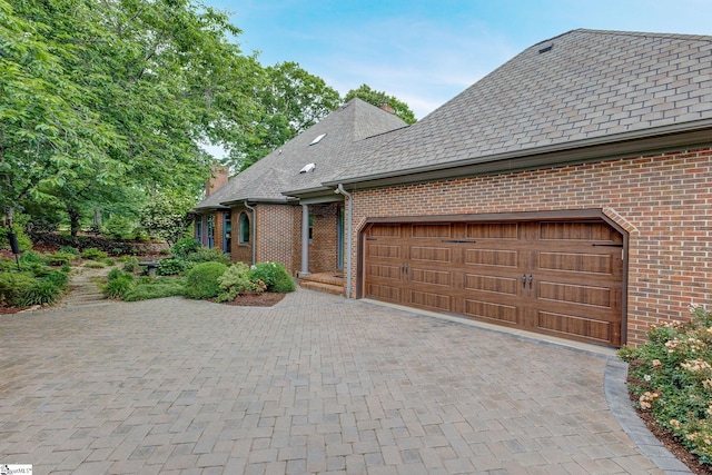 view of front of house featuring brick siding, a chimney, driveway, and a garage