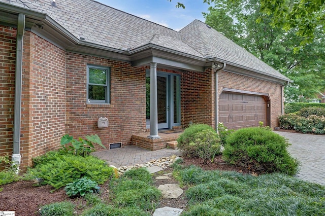 view of side of property with an attached garage, brick siding, driveway, and a high end roof