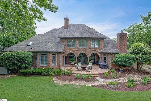 rear view of house with a lawn, a chimney, a patio area, and brick siding