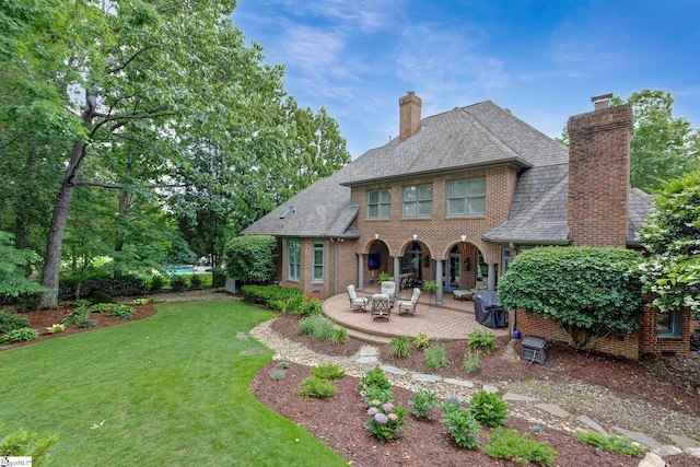 back of house featuring a chimney, a lawn, brick siding, and a patio area