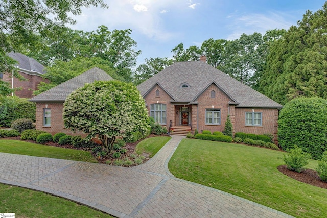 view of front of home featuring brick siding, a chimney, a front yard, and a shingled roof