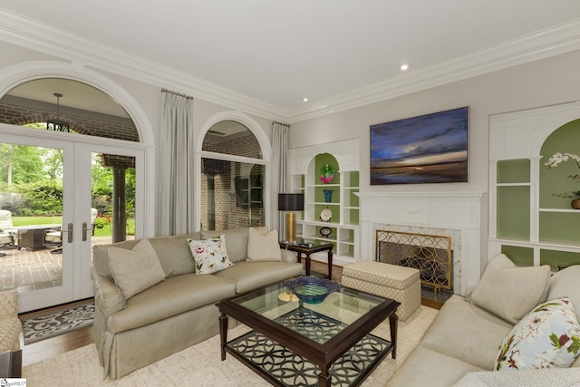 living room featuring french doors, crown molding, built in shelves, wood finished floors, and a fireplace