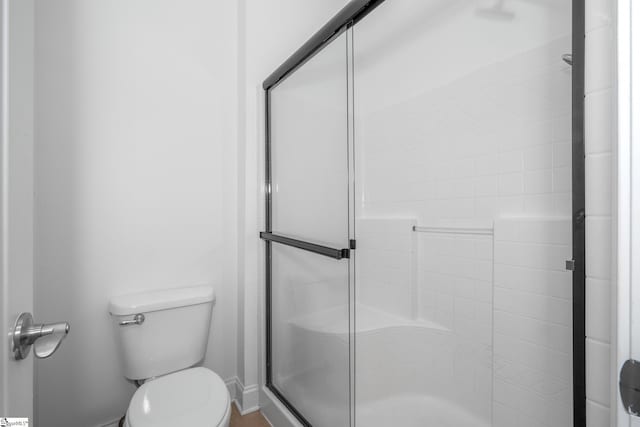 bathroom with a shower stall, toilet, and baseboards