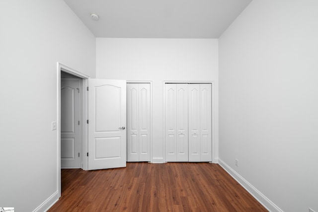 unfurnished bedroom featuring multiple closets, baseboards, and dark wood-style floors