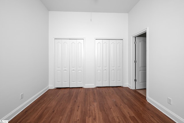 unfurnished bedroom featuring two closets, dark wood finished floors, baseboards, and a high ceiling