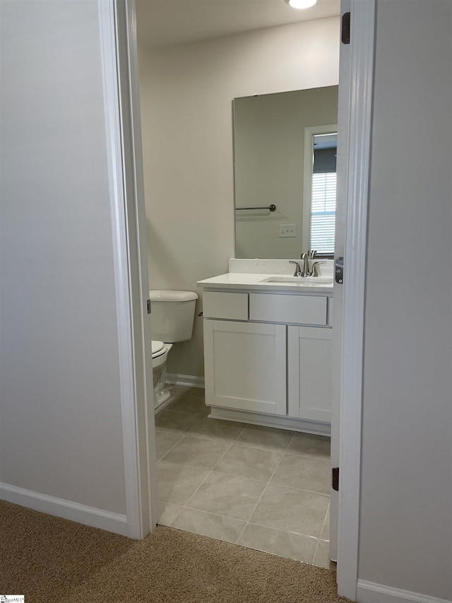 half bathroom with baseboards, vanity, toilet, and tile patterned flooring