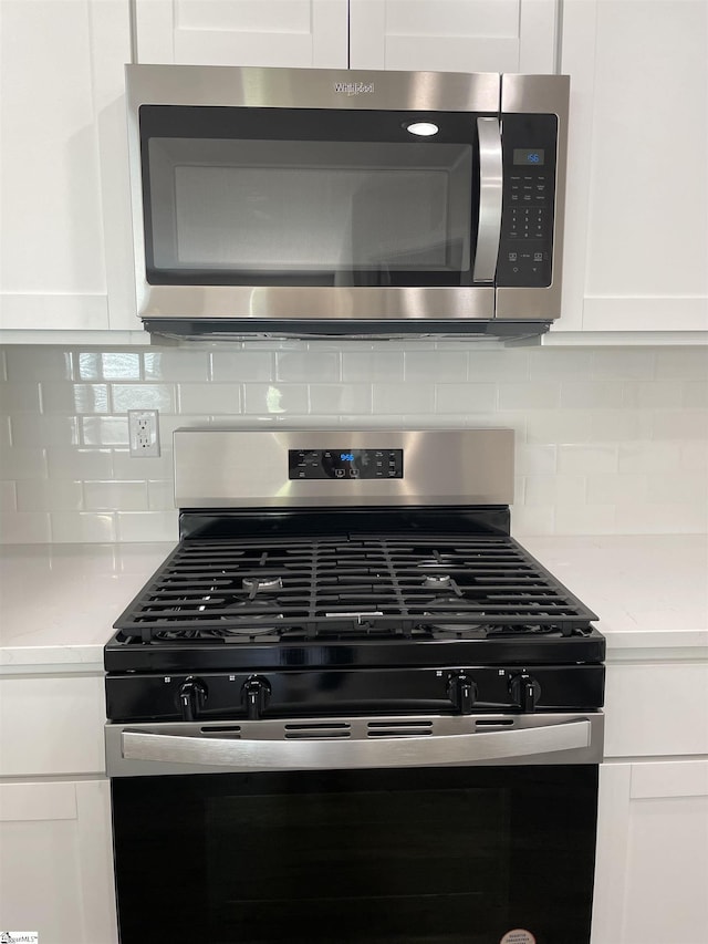 kitchen view of appliances with stainless steel finishes, white cabinetry, light stone counters, and tasteful backsplash