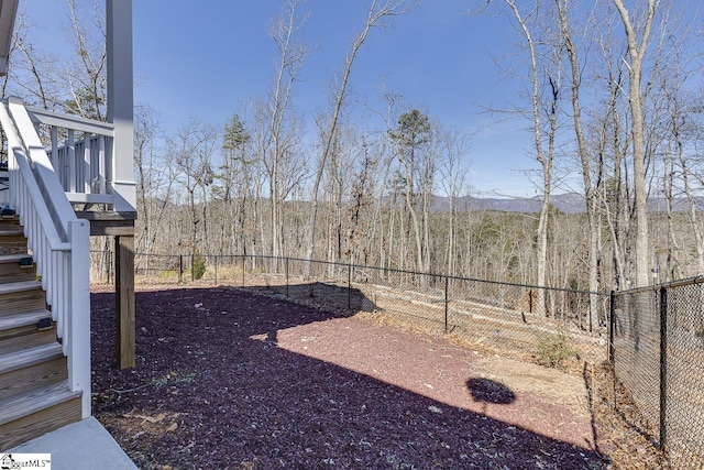 fenced backyard featuring stairway, a forest view, and a mountain view