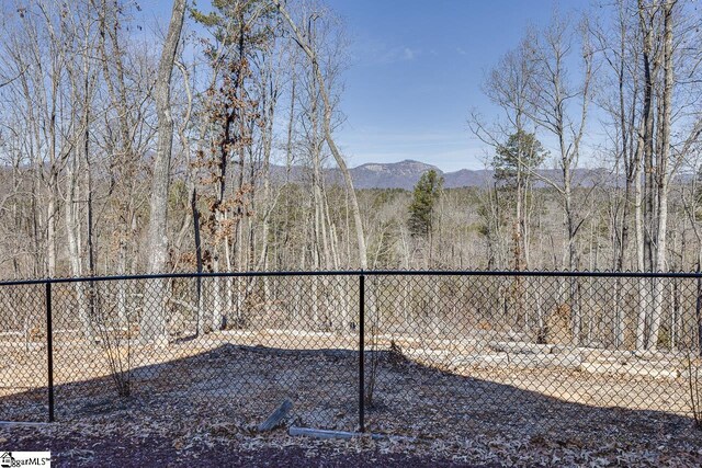 view of yard featuring fence, a mountain view, and a view of trees