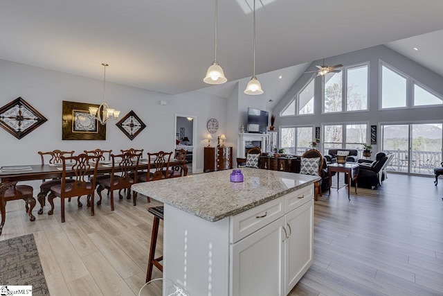 kitchen featuring light wood-style flooring, a kitchen island, ceiling fan, a fireplace, and high vaulted ceiling