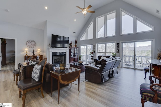 living area with high vaulted ceiling, a fireplace, ceiling fan, plenty of natural light, and light wood-style flooring