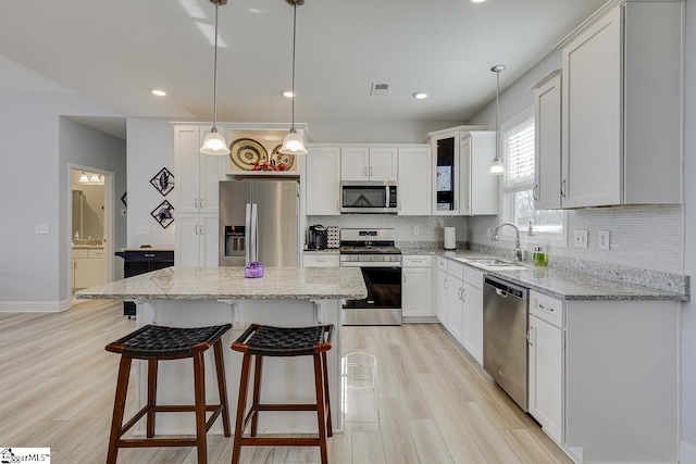 kitchen with appliances with stainless steel finishes, light wood-style flooring, tasteful backsplash, a sink, and white cabinetry