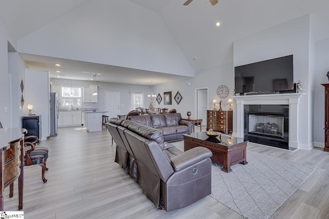 living room featuring high vaulted ceiling, light wood-style flooring, ceiling fan, a fireplace with flush hearth, and recessed lighting