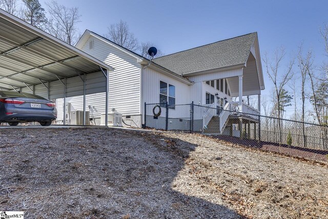 view of side of home featuring fence, a carport, and a shingled roof