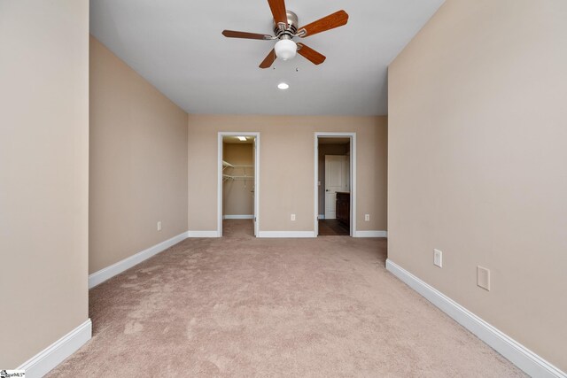 unfurnished bedroom with a spacious closet, carpet, baseboards, a closet, and a ceiling fan