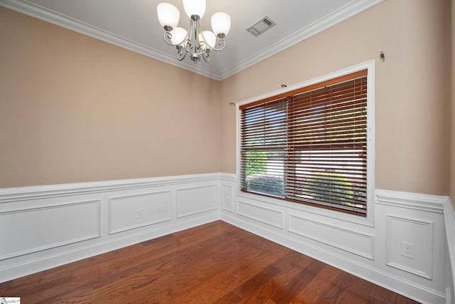empty room with a chandelier, crown molding, dark wood finished floors, and a wainscoted wall