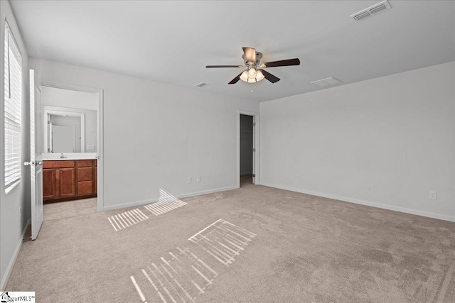 unfurnished bedroom with light colored carpet, baseboards, ensuite bathroom, and a ceiling fan