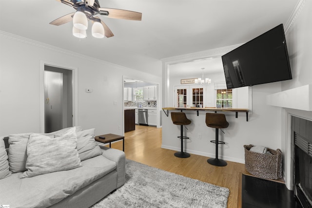living room featuring light wood-style flooring, ornamental molding, ceiling fan, a chandelier, and baseboards