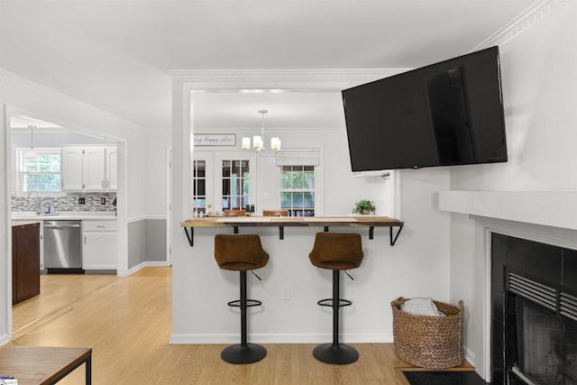 kitchen with dishwasher, a breakfast bar area, light wood-style flooring, a chandelier, and healthy amount of natural light