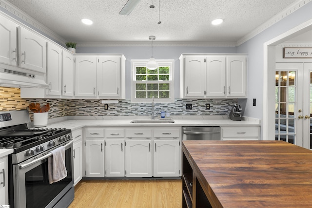 kitchen with stainless steel appliances, a sink, under cabinet range hood, a textured ceiling, and wood counters