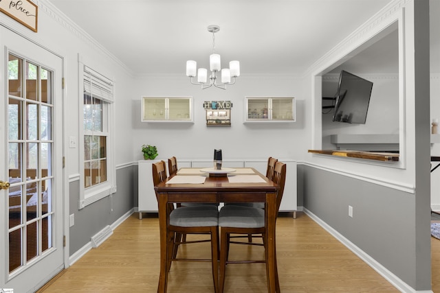 dining space featuring a chandelier, light wood finished floors, crown molding, and baseboards