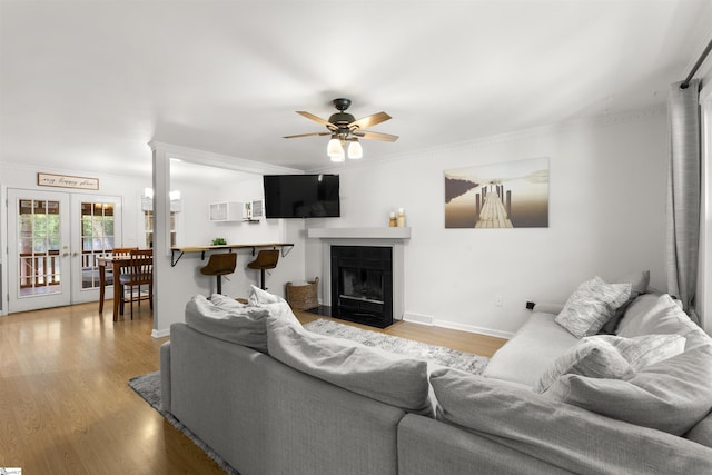 living area with ceiling fan, light wood-type flooring, ornamental molding, baseboards, and a fireplace with flush hearth
