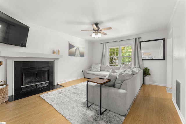 living area with a fireplace, a ceiling fan, wood finished floors, and ornamental molding