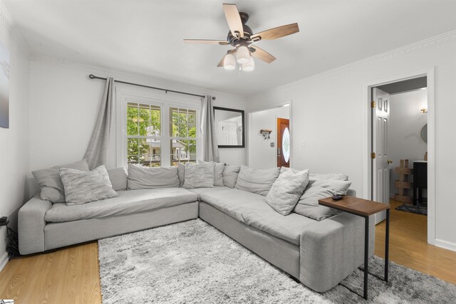 living area with a ceiling fan, light wood finished floors, a wood stove, crown molding, and baseboards