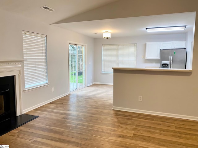 unfurnished living room featuring light wood-style floors, baseboards, a fireplace with raised hearth, and vaulted ceiling