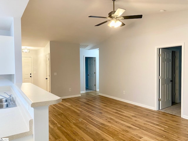 unfurnished living room featuring ceiling fan, a sink, light wood-type flooring, baseboards, and vaulted ceiling