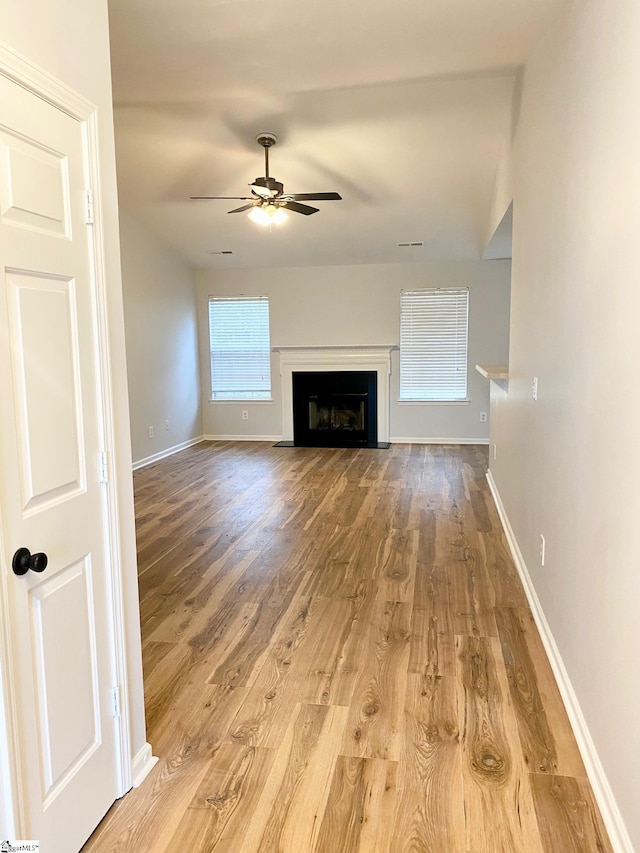 unfurnished living room featuring ceiling fan, wood finished floors, baseboards, and a fireplace