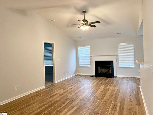 unfurnished living room featuring a ceiling fan, wood finished floors, vaulted ceiling, baseboards, and a fireplace with flush hearth