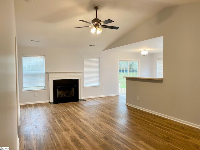 unfurnished living room featuring wood finished floors, lofted ceiling, a ceiling fan, baseboards, and a fireplace with flush hearth